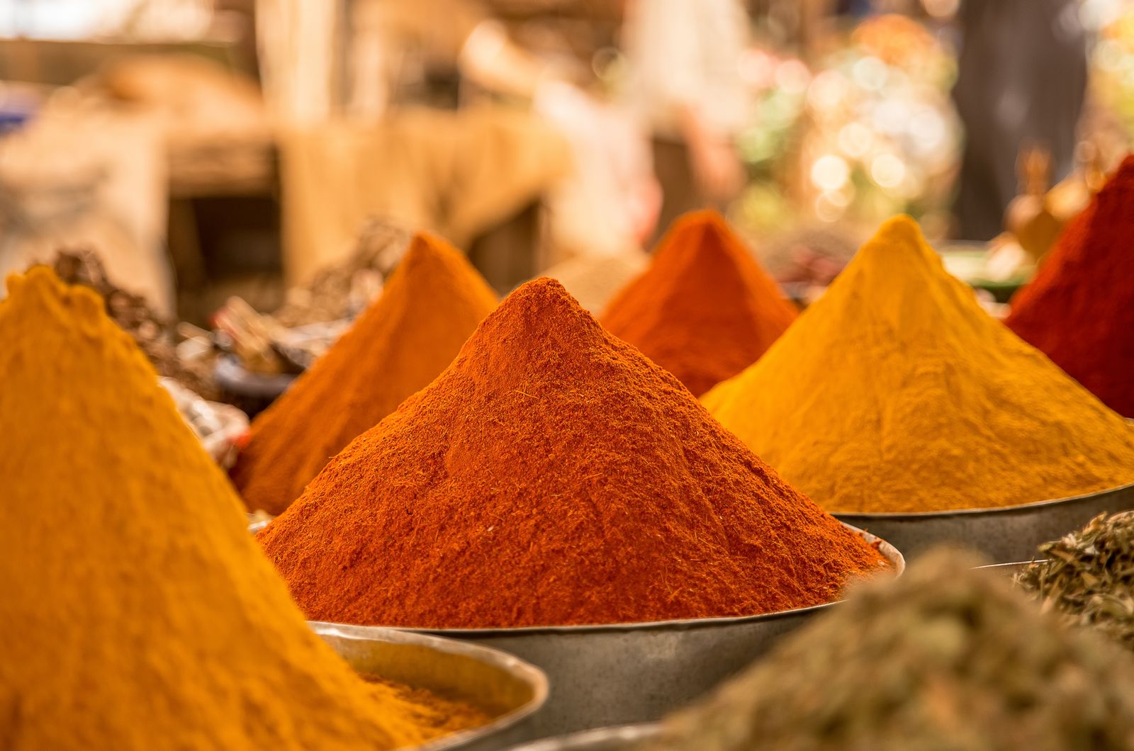 Cones of ground turmeric, paprika and curry powder in bowls at a spice stall
