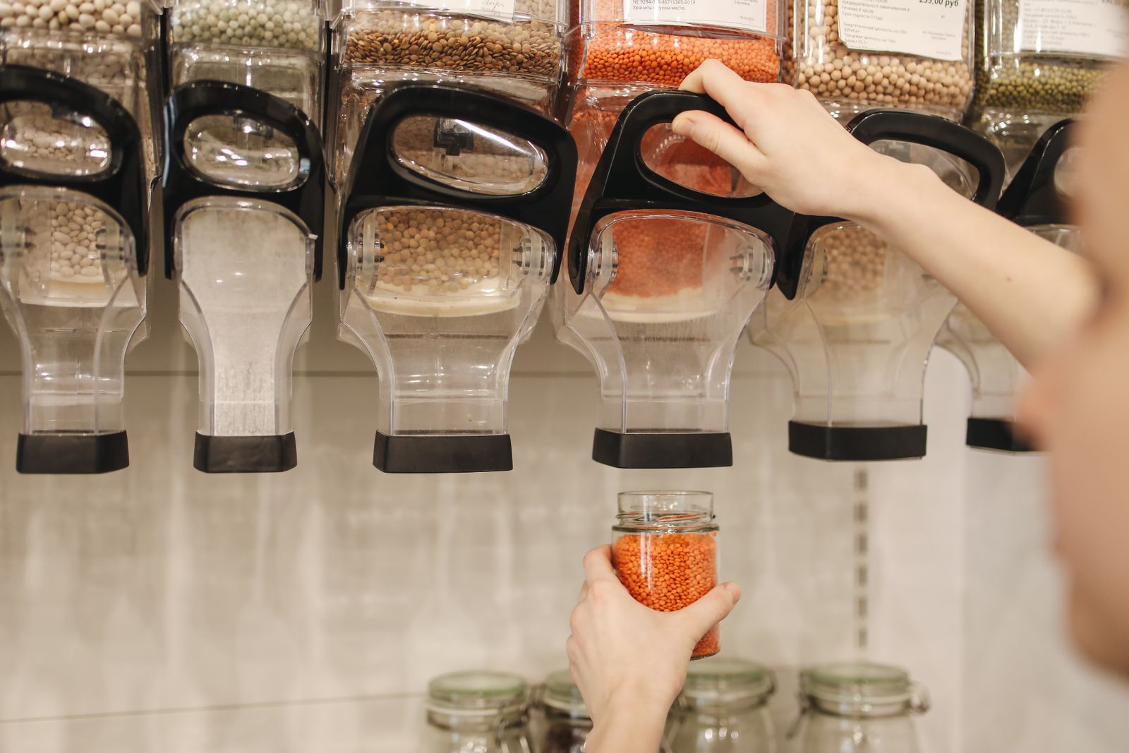 A shopper filling a glass jar with lentils from a gravity dispenser