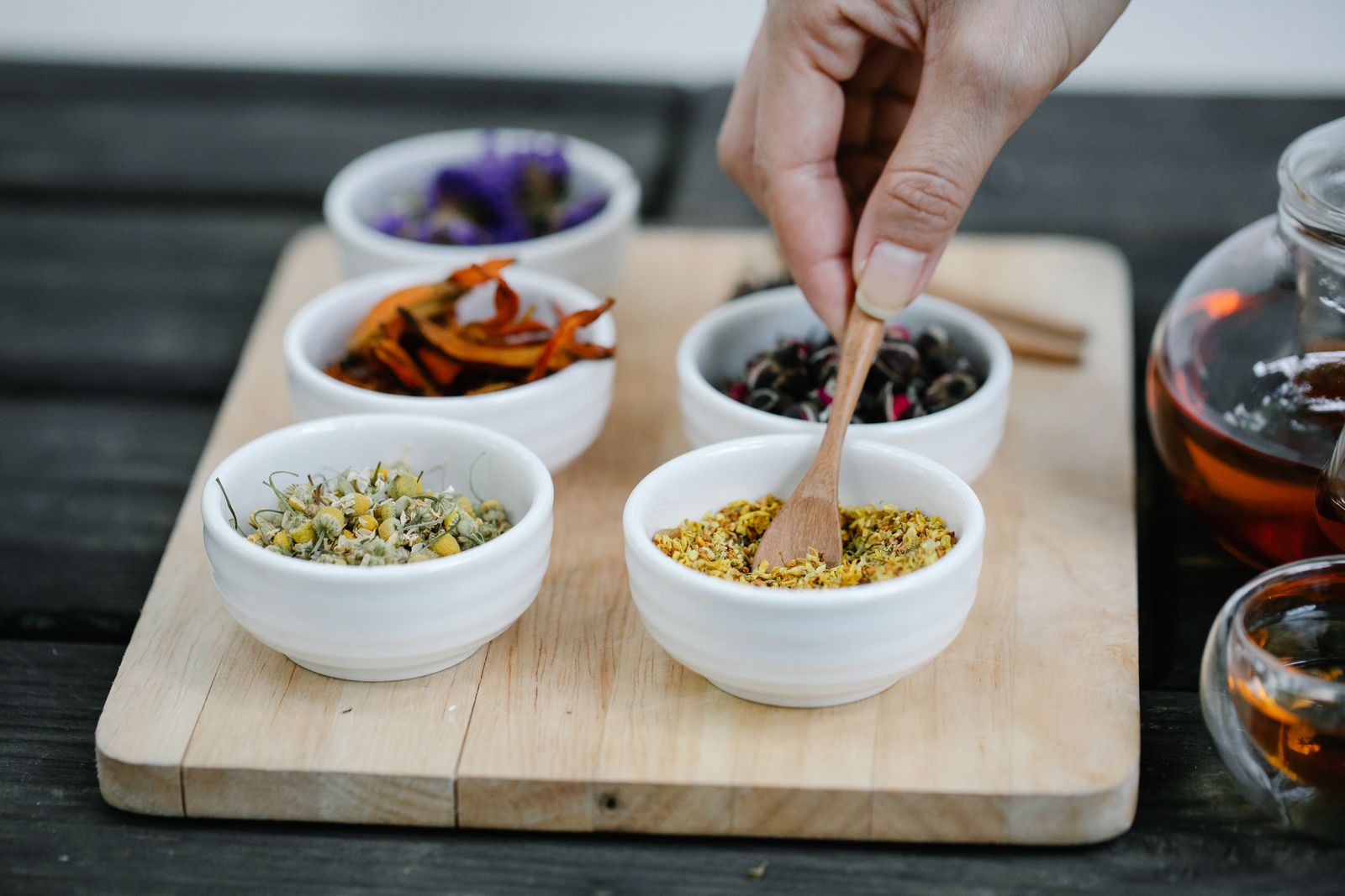 A hand taking dried spices from small white bowls on a wooden tray