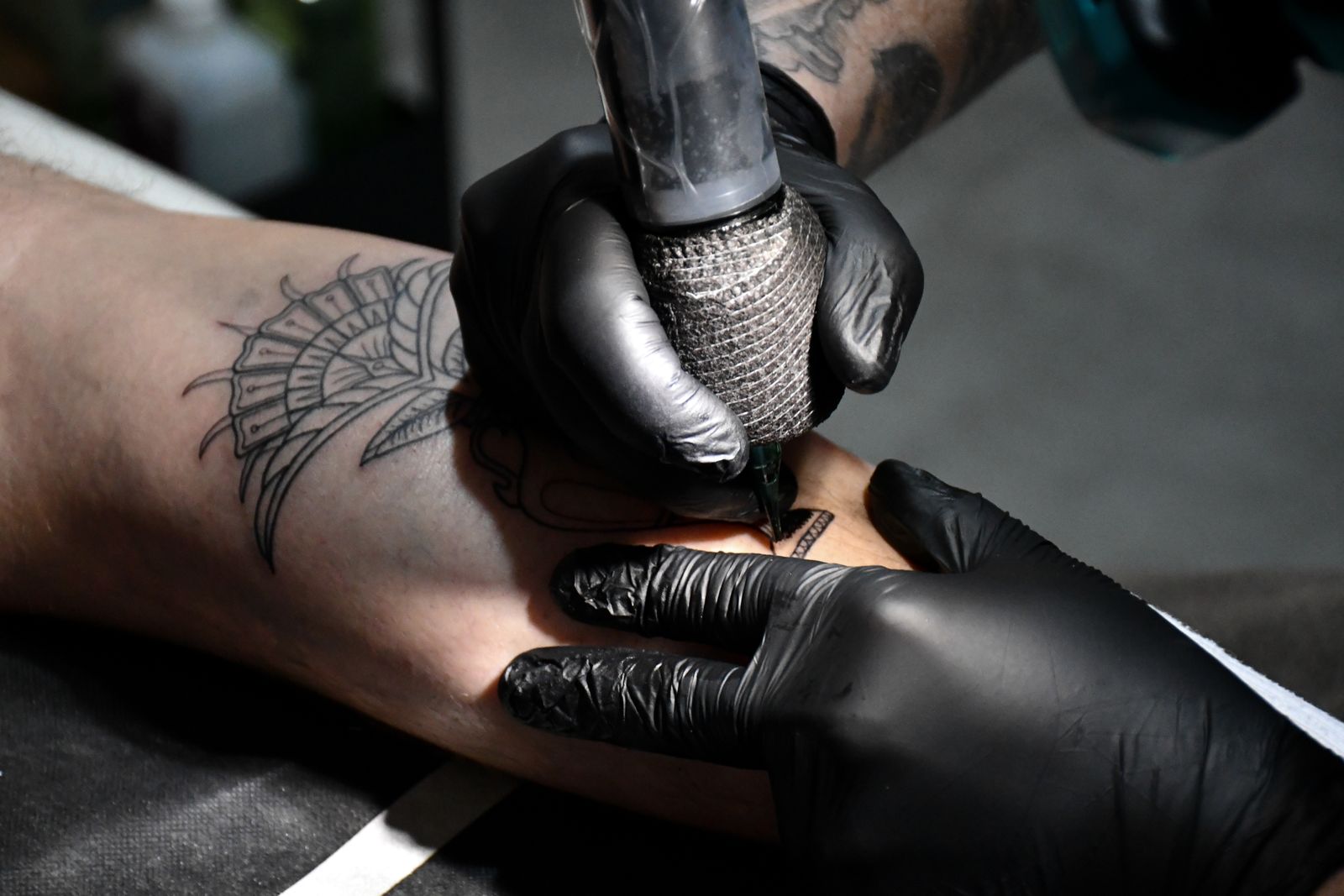 Gloved hands tattooing a fine line design on a forearm