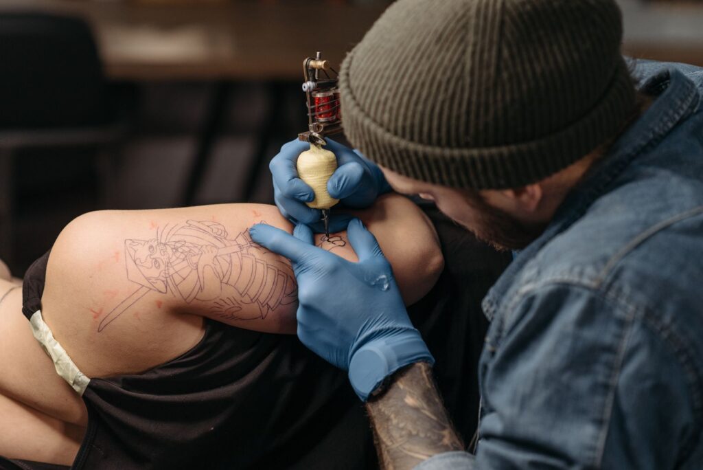 A tattoo artist in a beanie working on a client's shoulder