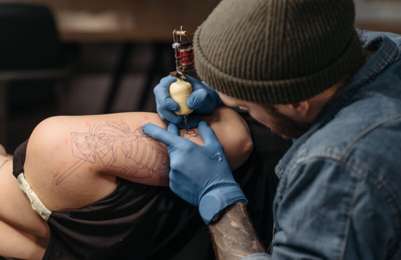 A tattoo artist in a beanie working on a client's shoulder