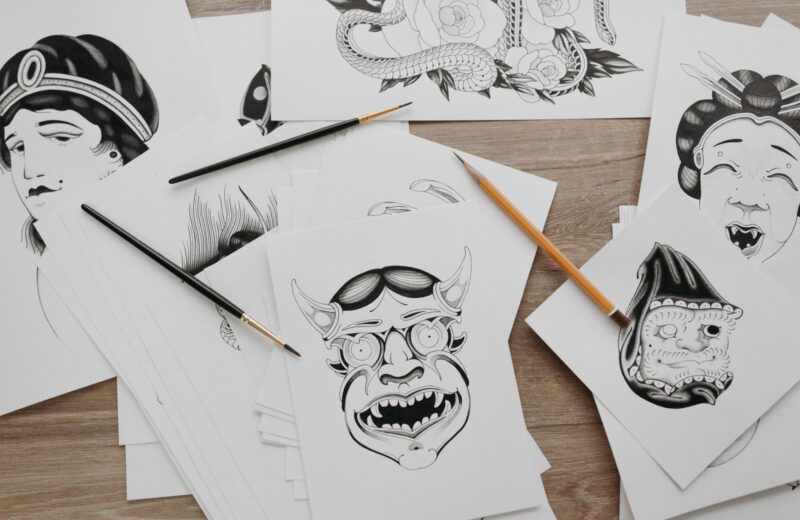 Traditional tattoo designs drawn on paper, with brushes and pencils beside them