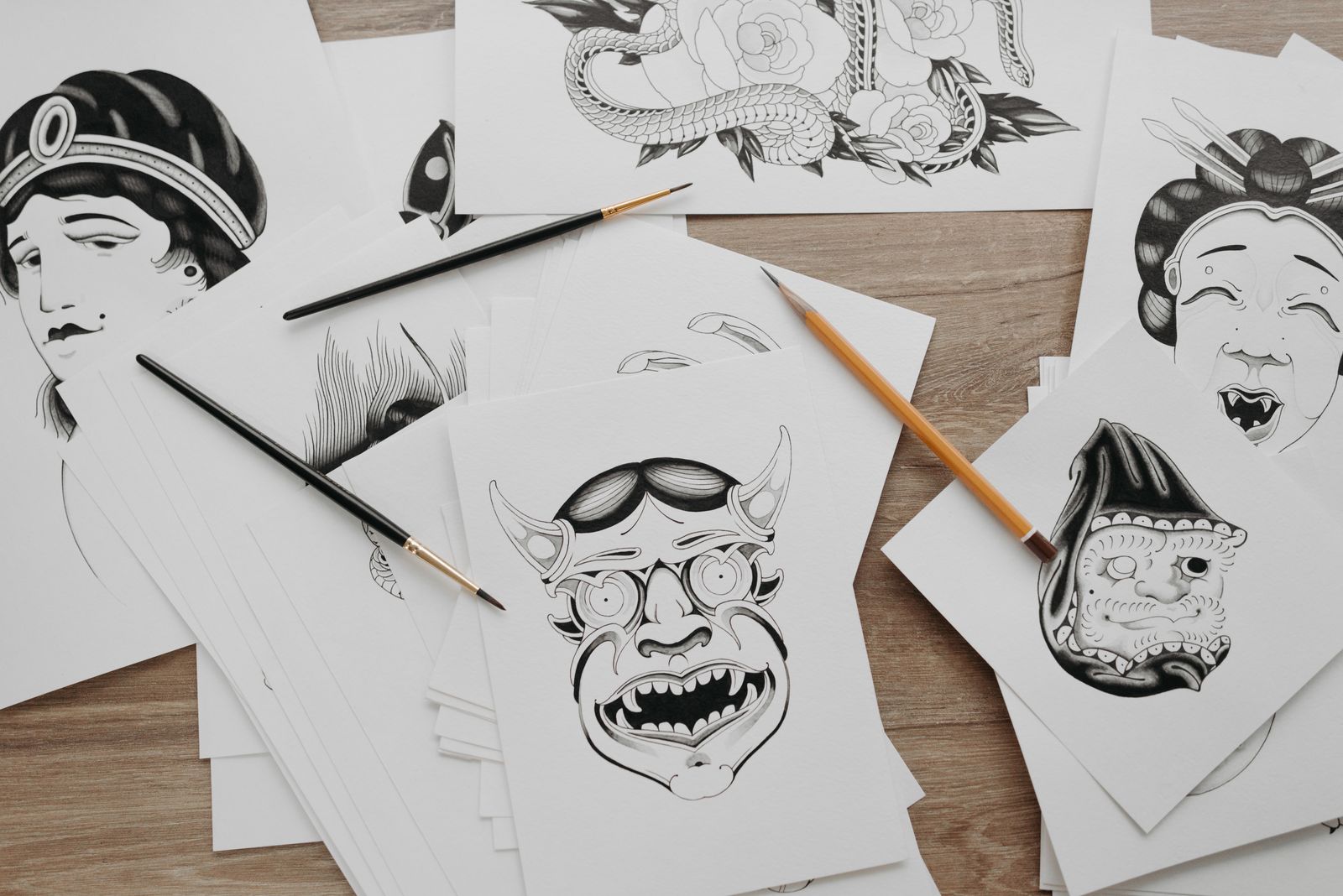 Traditional tattoo designs drawn on paper, with brushes and pencils beside them
