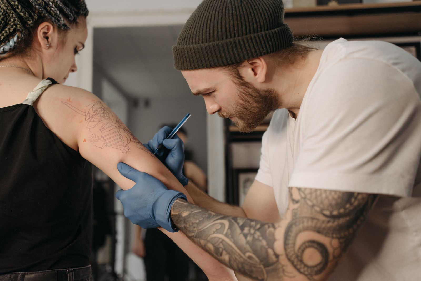 A tattoo artist in blue gloves working on a client's upper arm in a bright studio