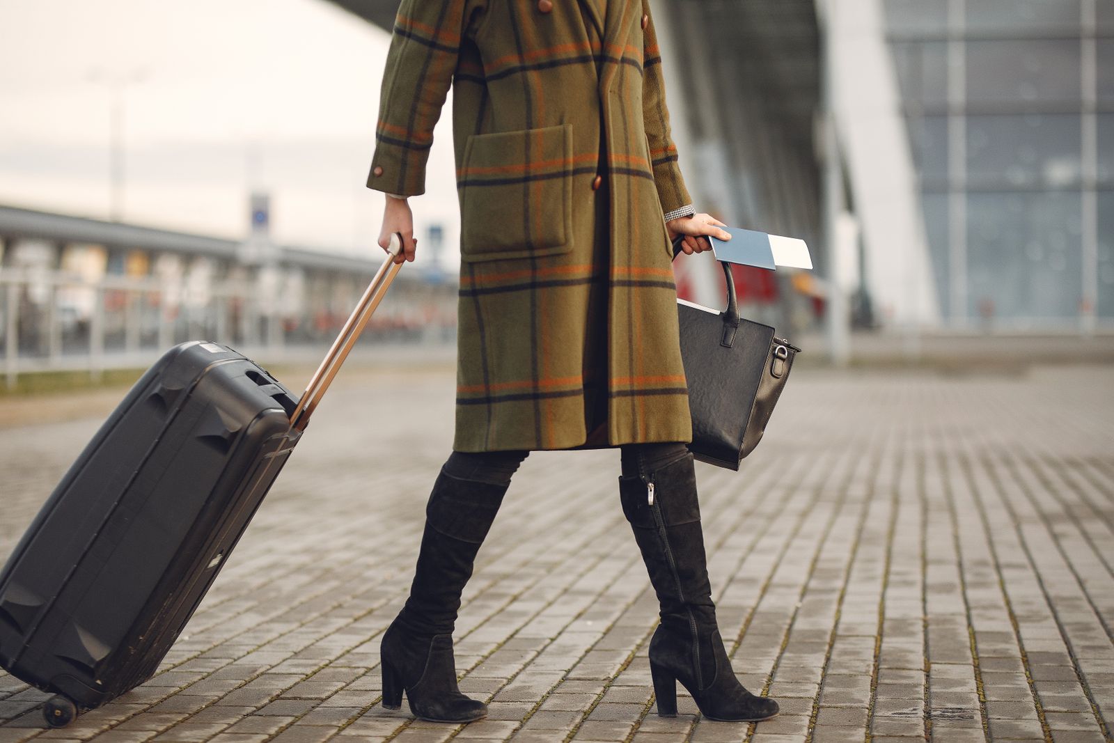 A traveller pulling a black suitcase across the pavement outside an airport terminal