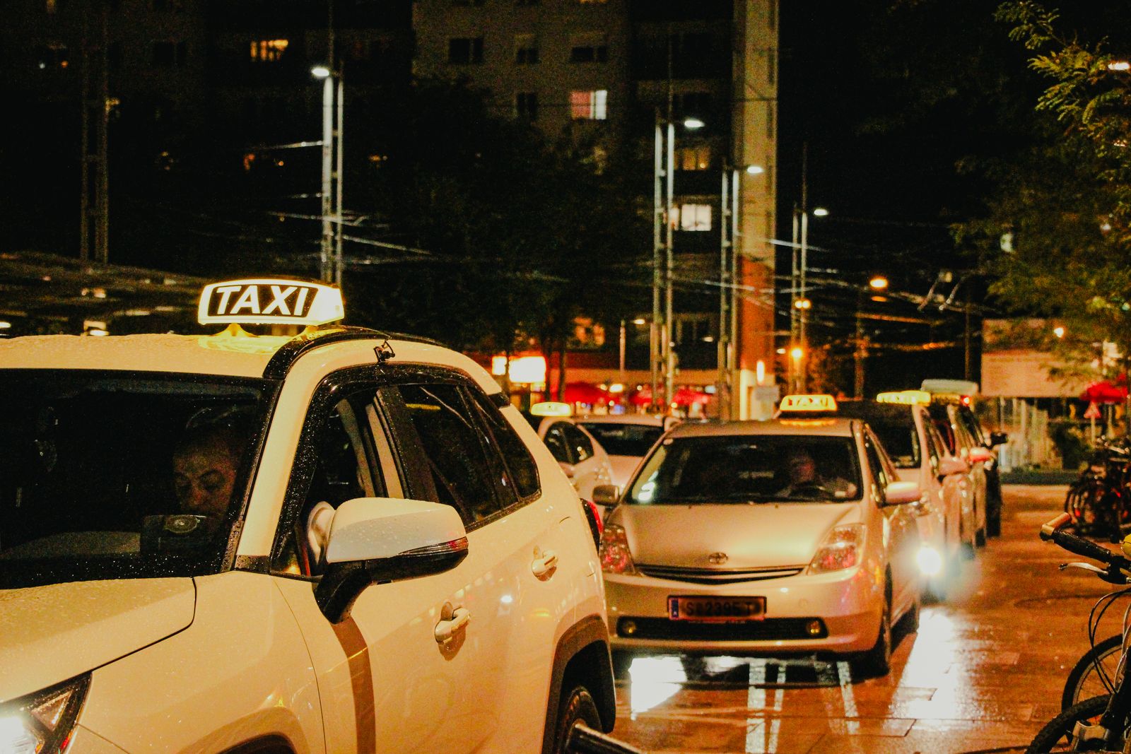 White taxis waiting in line at a rank at night, roof signs lit
