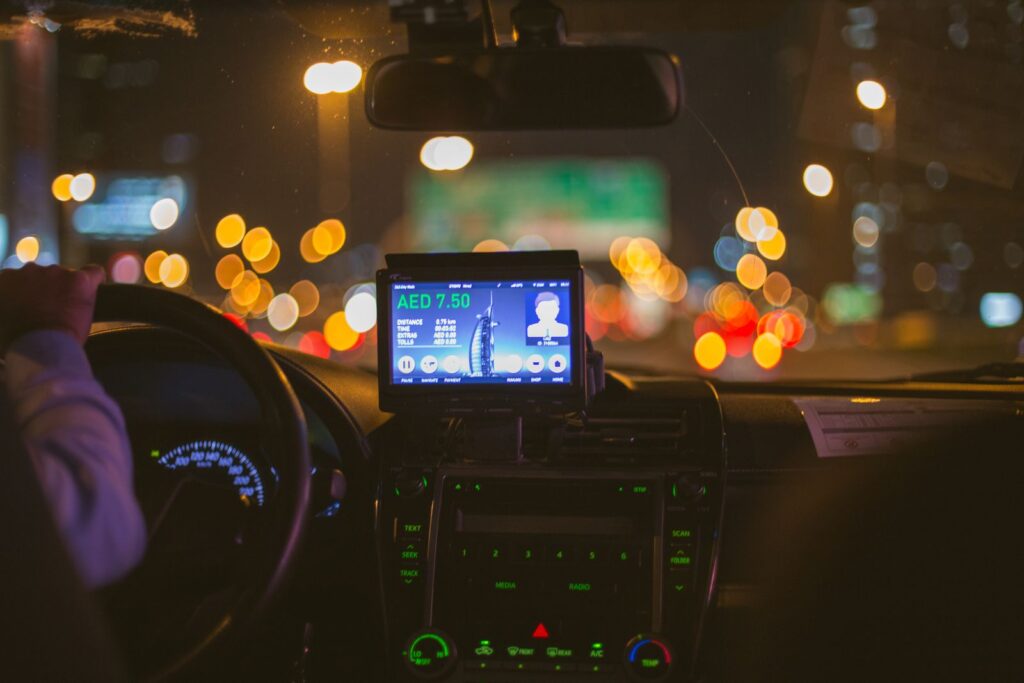 The dashboard of a taxi at night with city lights blurred through the windscreen