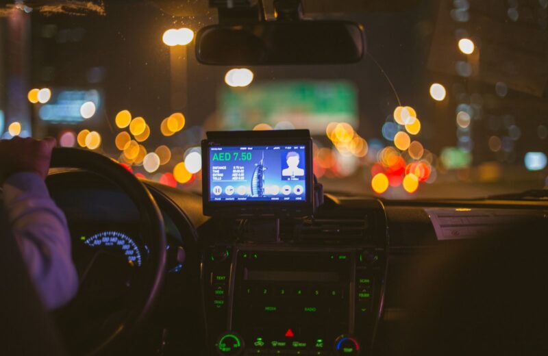 The dashboard of a taxi at night with city lights blurred through the windscreen