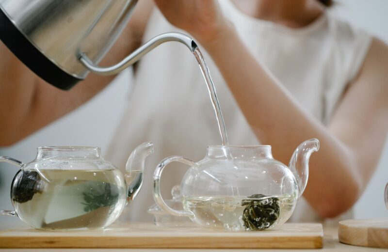 Hot water poured from a kettle into glass teapots of green tea
