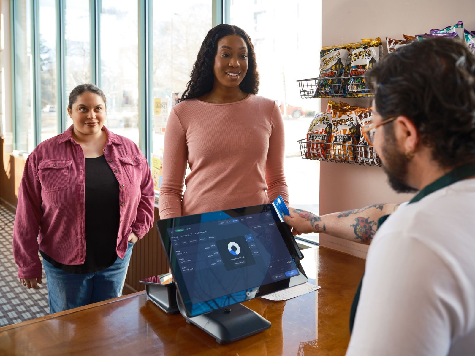 Two customers at a shop counter talking to a member of staff beside a tablet on a stand