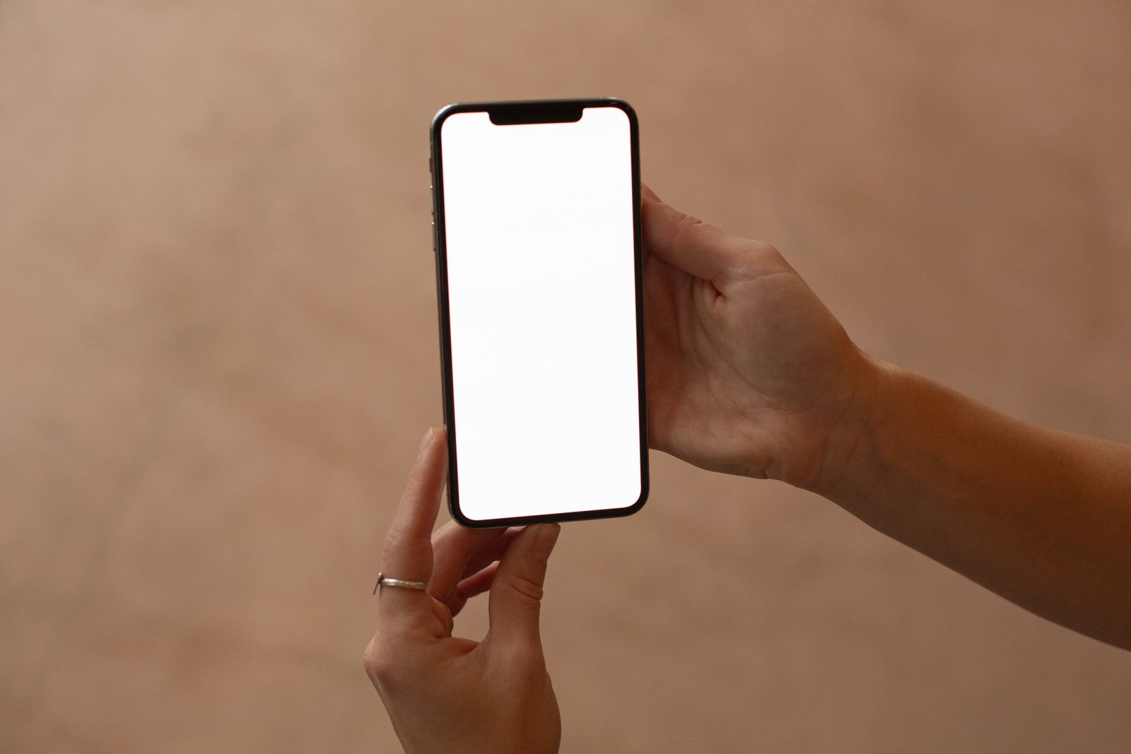 A hand holding a phone with a blank white screen against a warm beige wall