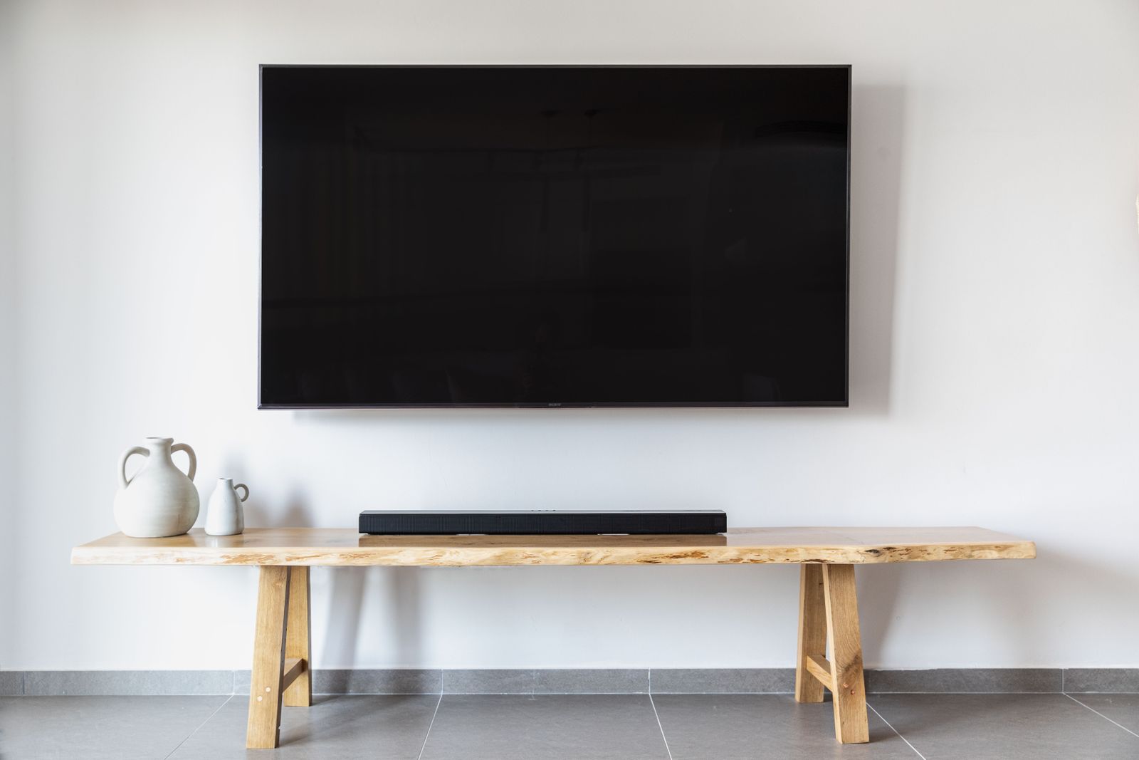 A flat TV mounted on a white living-room wall above a low wooden console with a soundbar