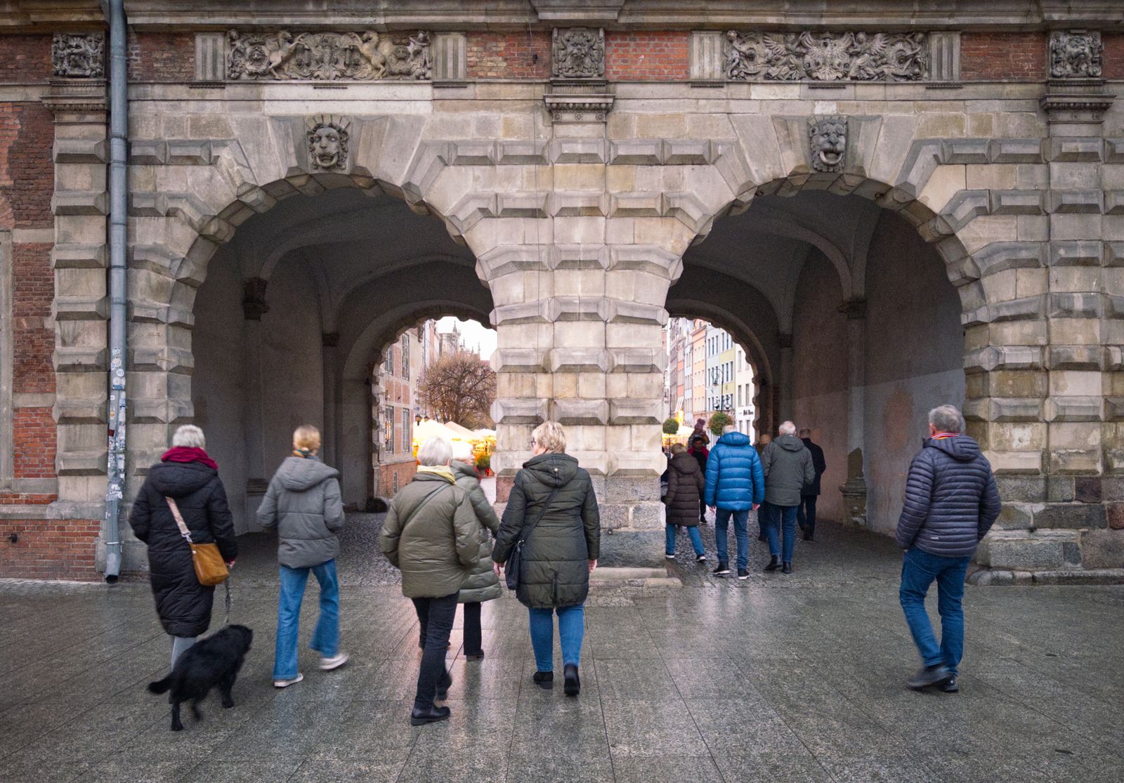 A small group of travellers walking through an old town gate, seen from behind