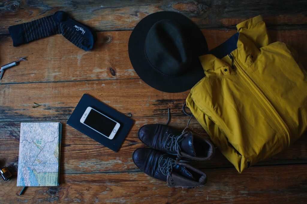 Travel clothes, shoes, a hat and a map laid out on a wooden table