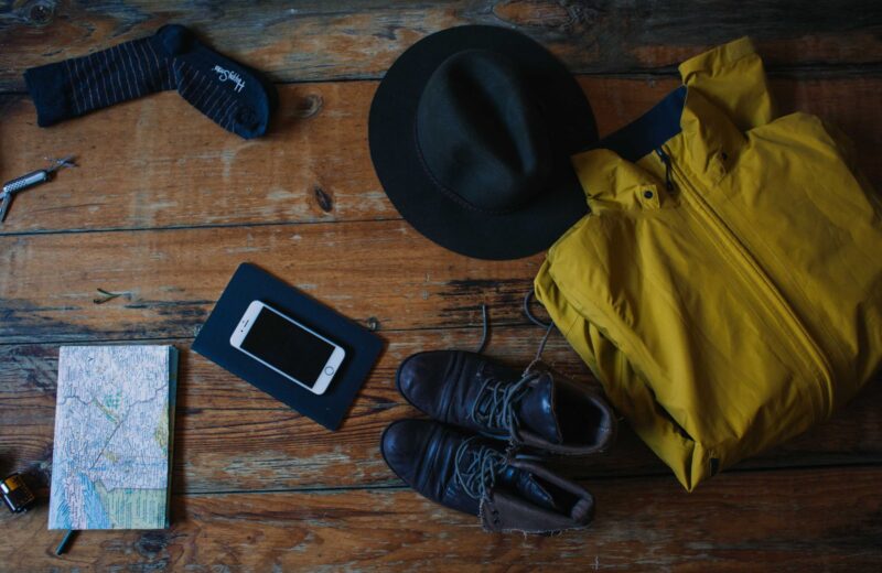 Travel clothes, shoes, a hat and a map laid out on a wooden table