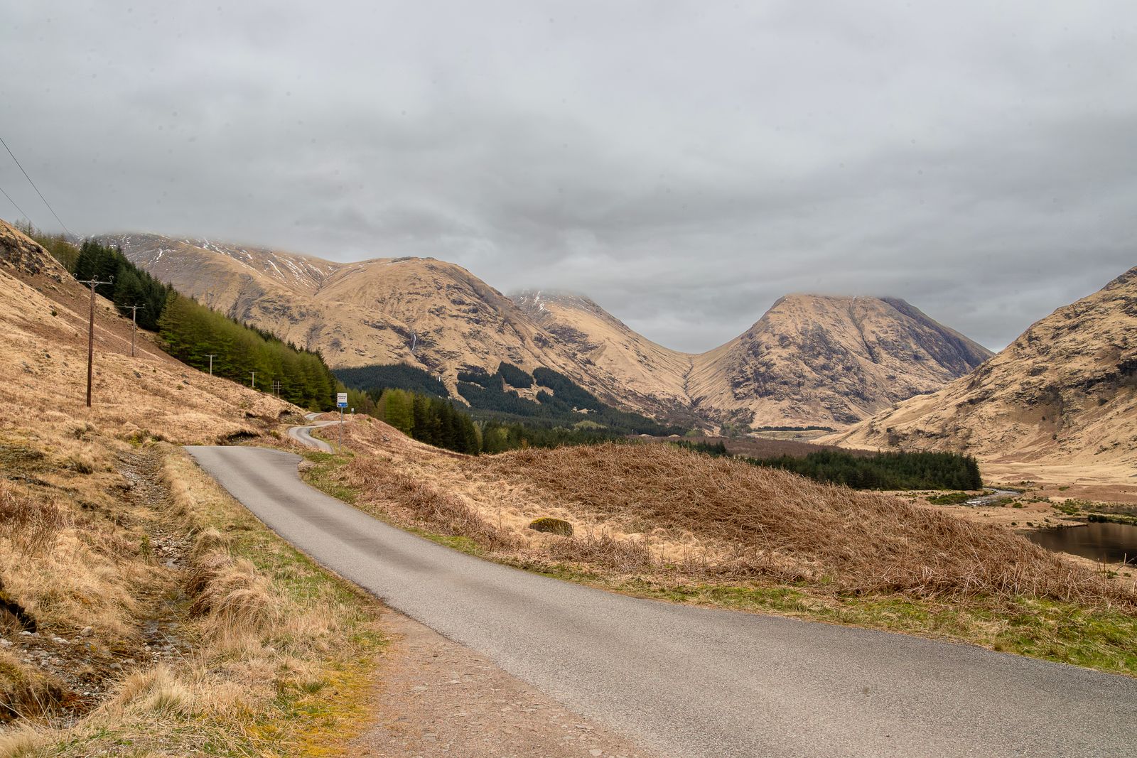 A single-track road through a Highland glen under grey clouds