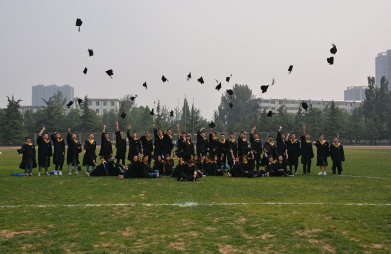 Graduates throwing their caps in the air on a lawn, seen from a distance