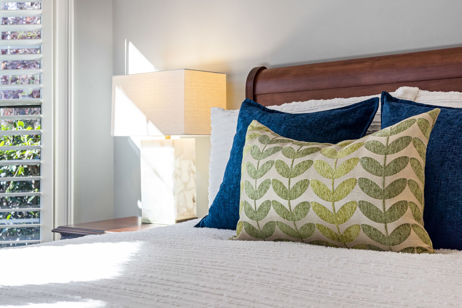 A made bed with blue and green cushions beside a bright window