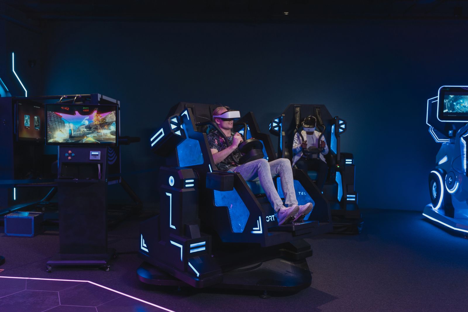 Two players in VR headsets on motion seats in a dim arcade hall