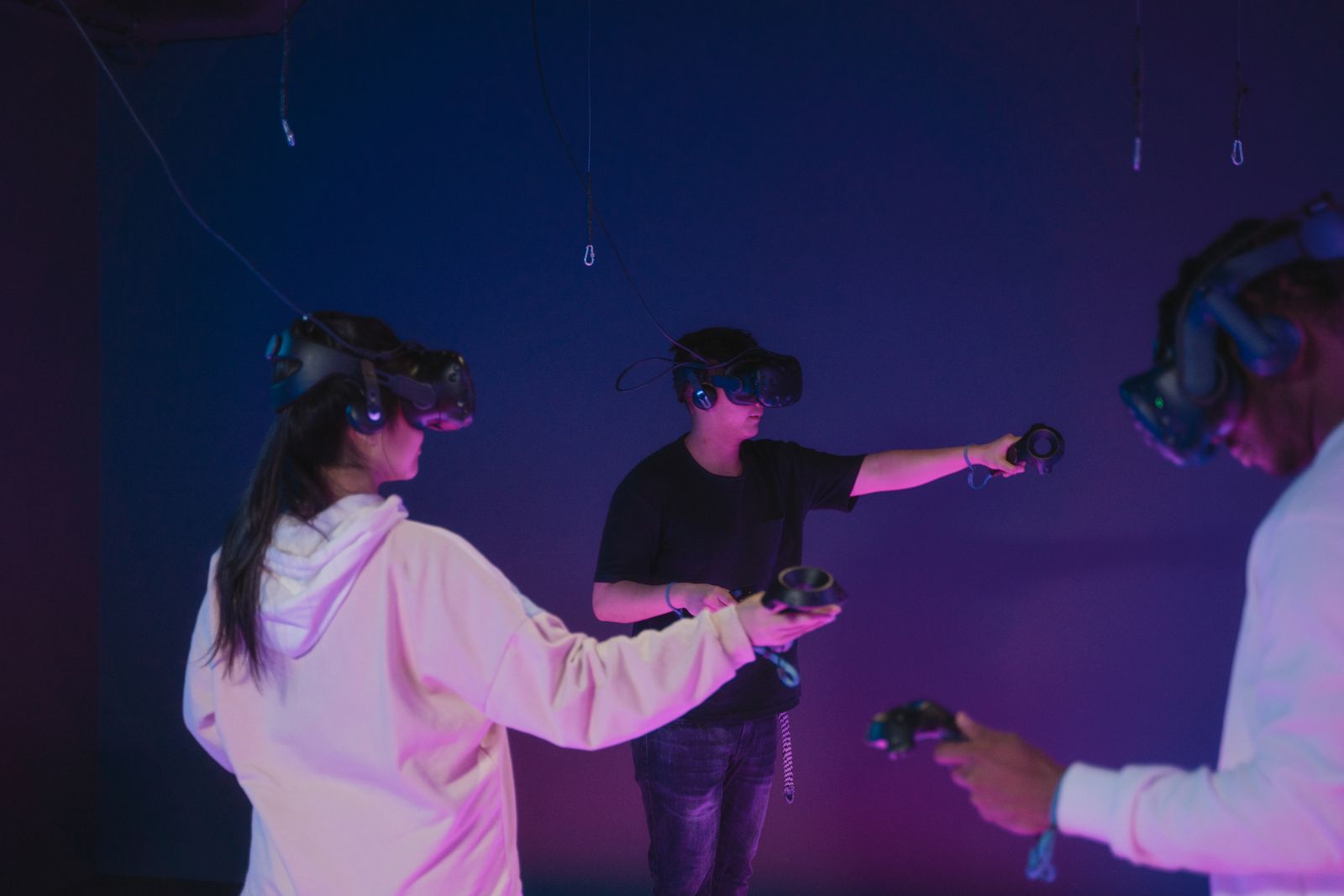 Three players in VR headsets with controllers in a dark free-roam arena