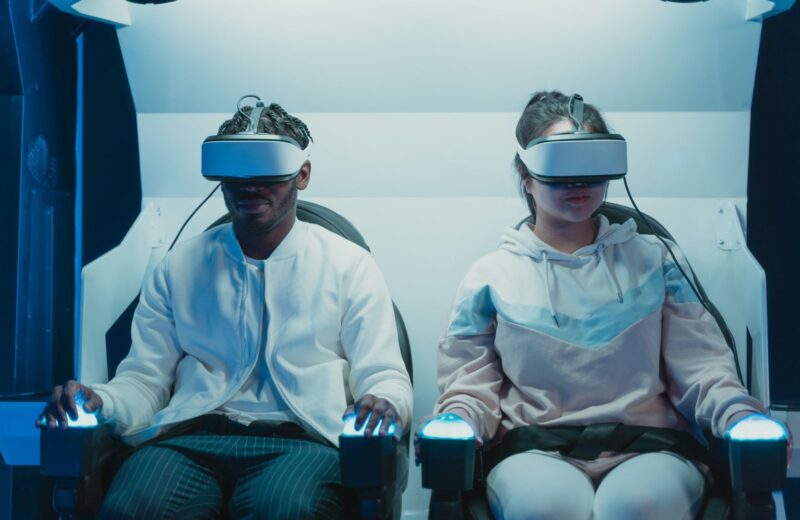 Two players in VR headsets in white seats in a VR arcade