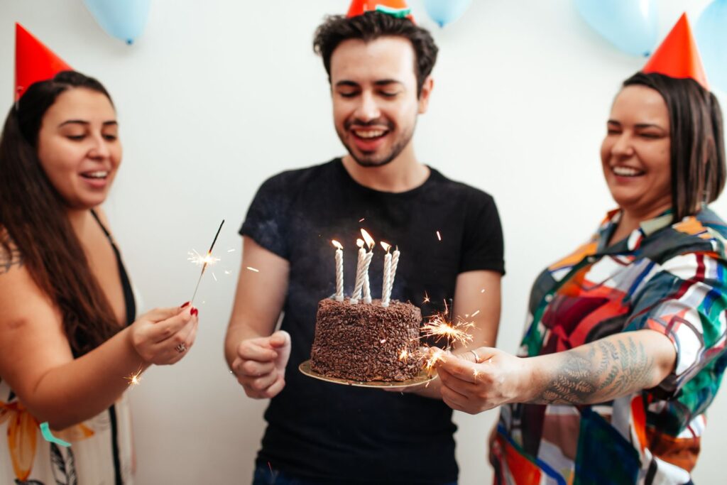 Three friends in party hats with a cake and sparklers