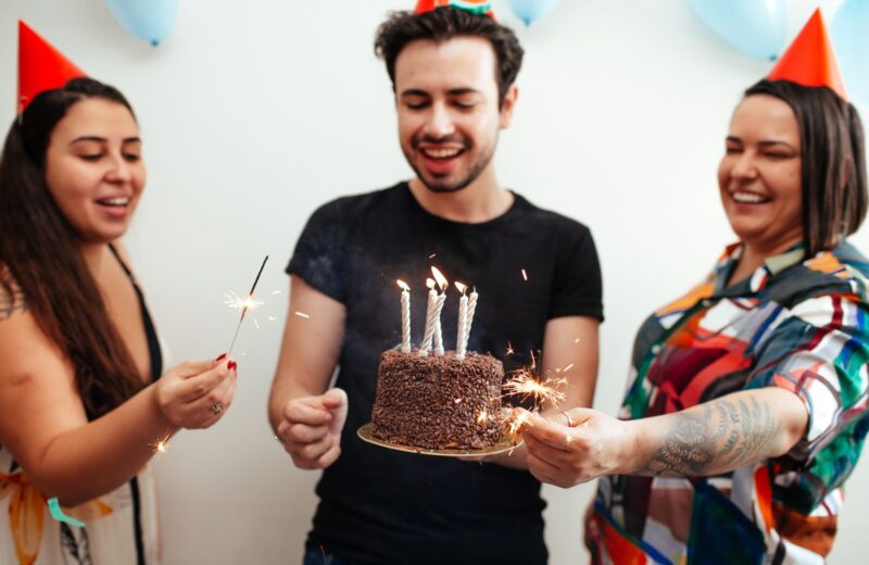 Three friends in party hats with a cake and sparklers