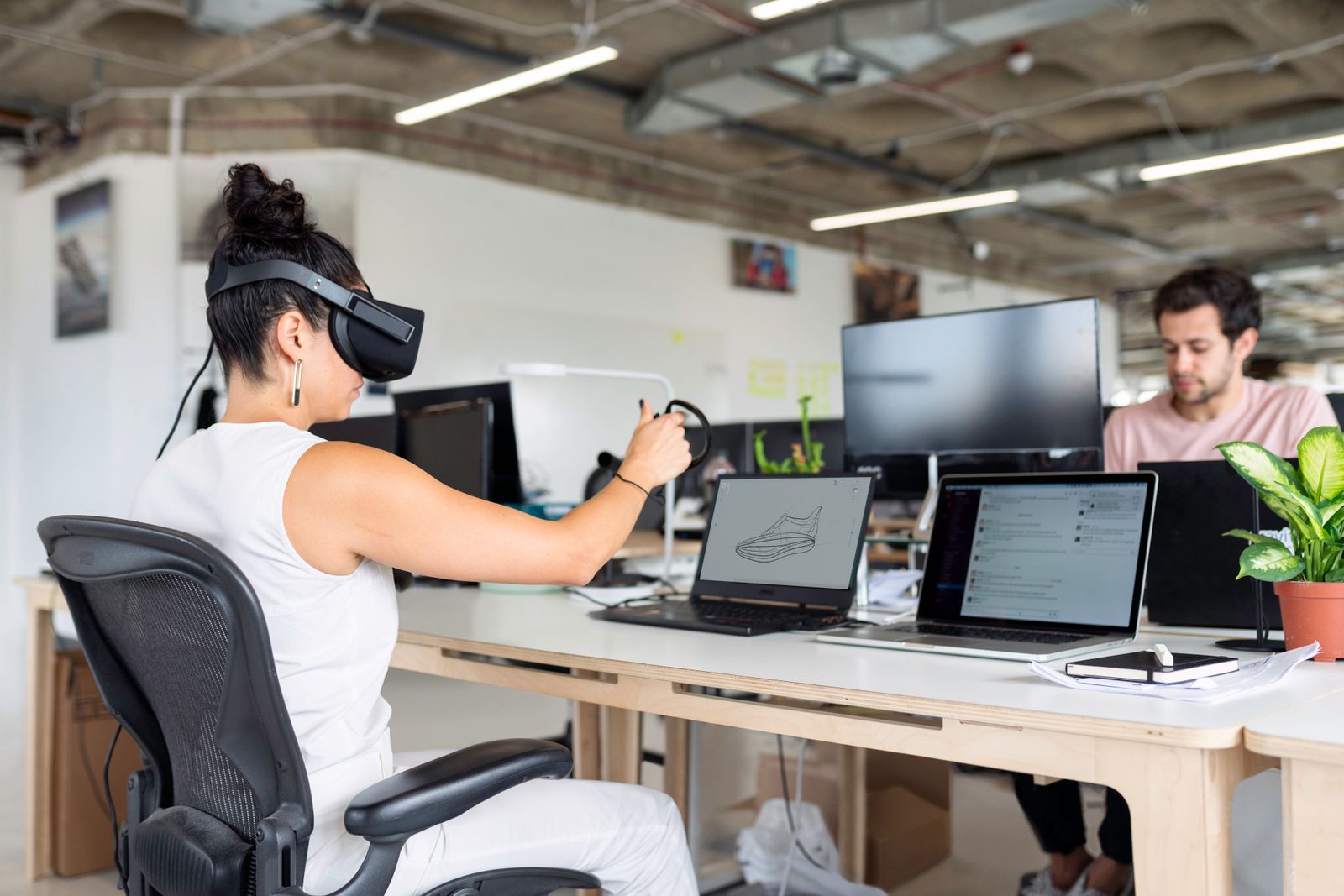 A designer in a VR headset reviewing a shoe model at an open-plan desk