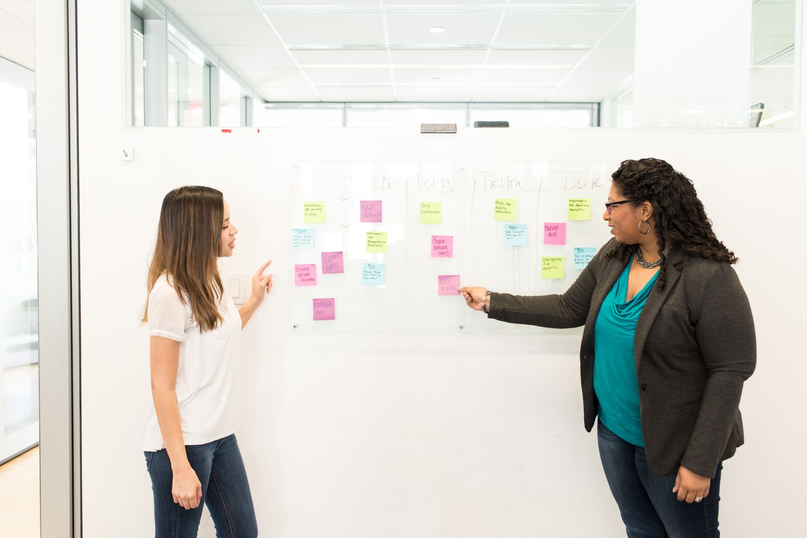 Two women sorting sticky notes on a whiteboard during a planning session