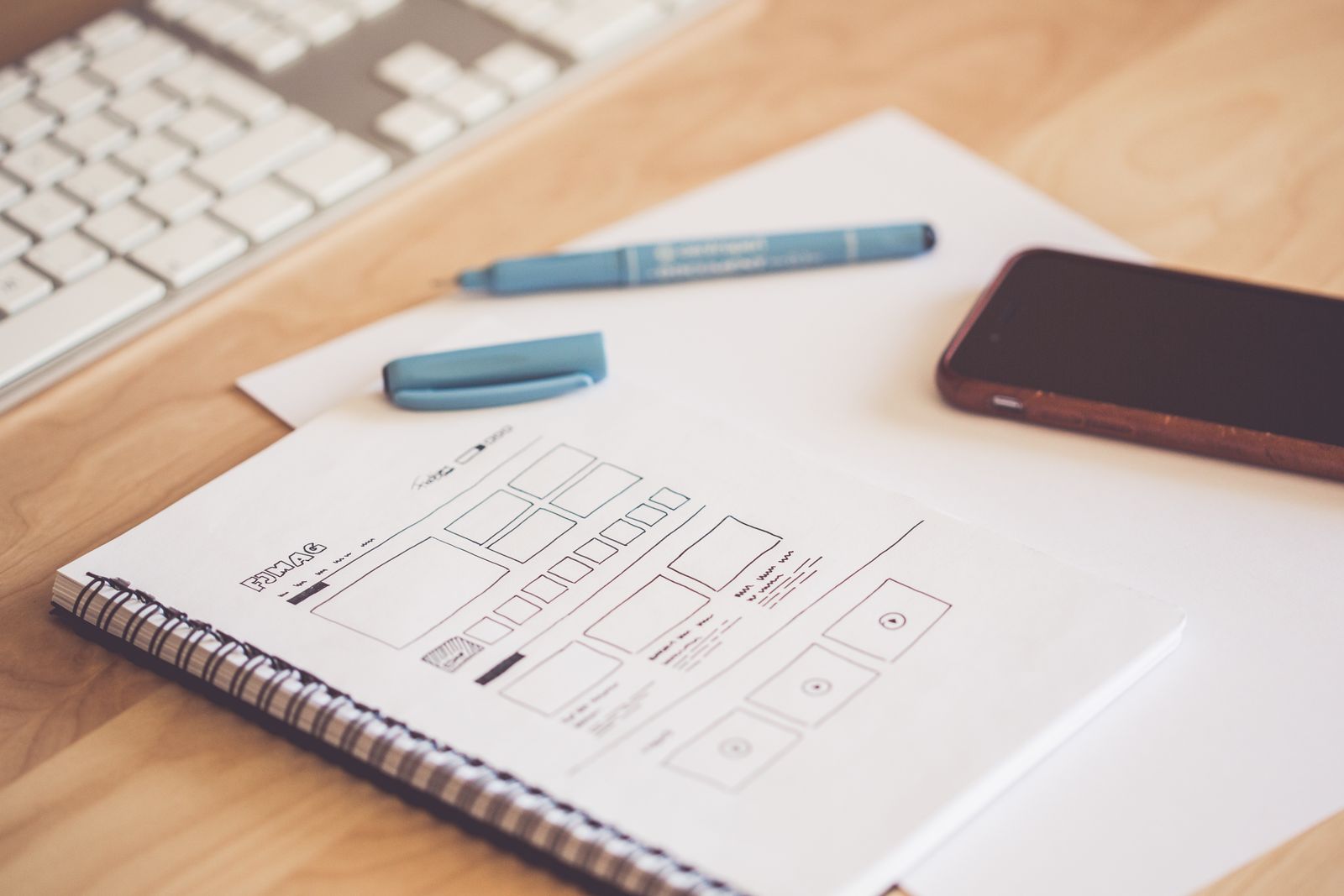Sketchpad with hand-drawn website wireframes beside a keyboard on a wooden desk