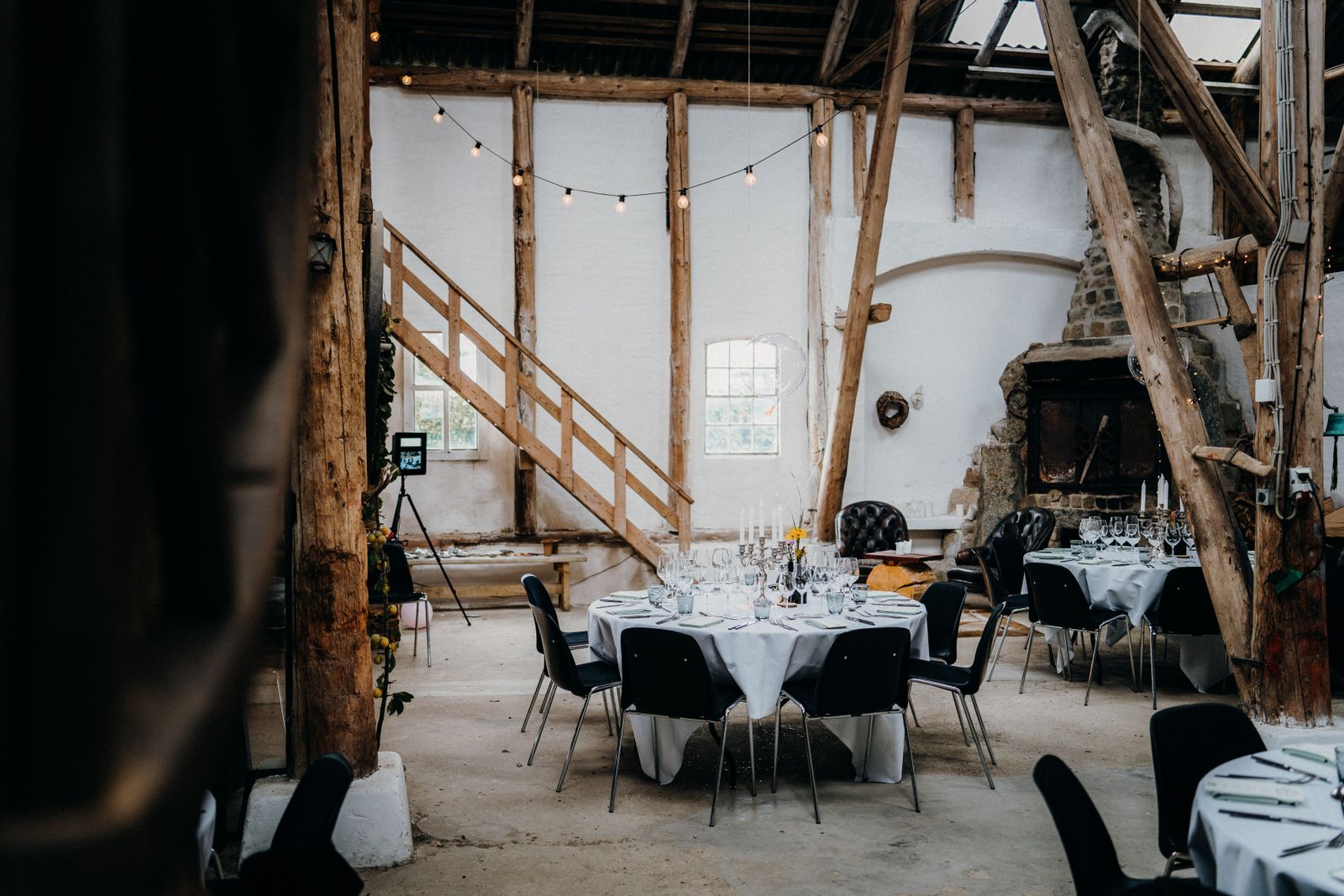 Round tables laid with white linen inside a timber barn