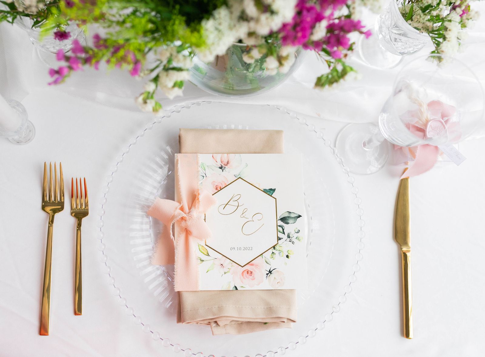 A menu card on a plate between gold cutlery and flowers