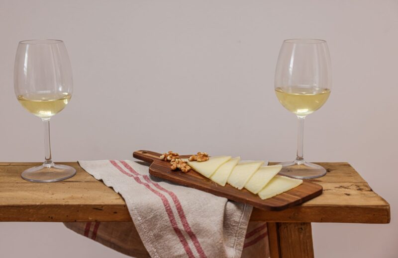 Two glasses of white wine with cheese and walnuts on a wooden board