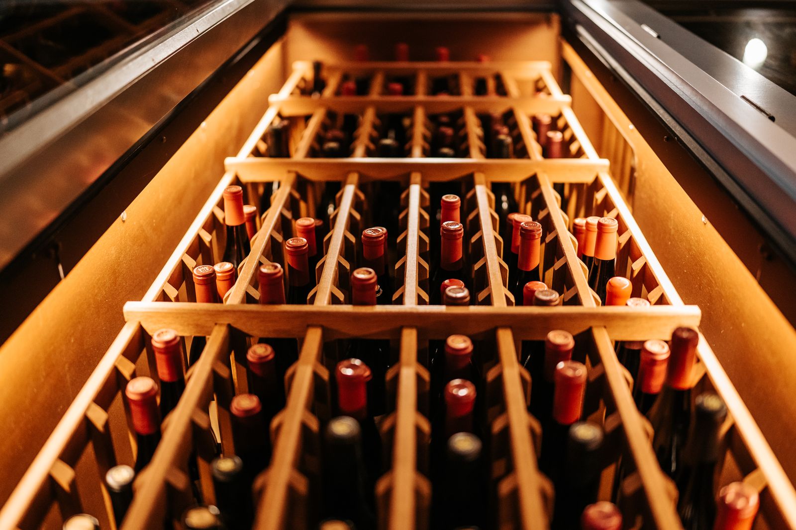 Bottles lying in a lit wooden wine rack, seen from the end of the aisle