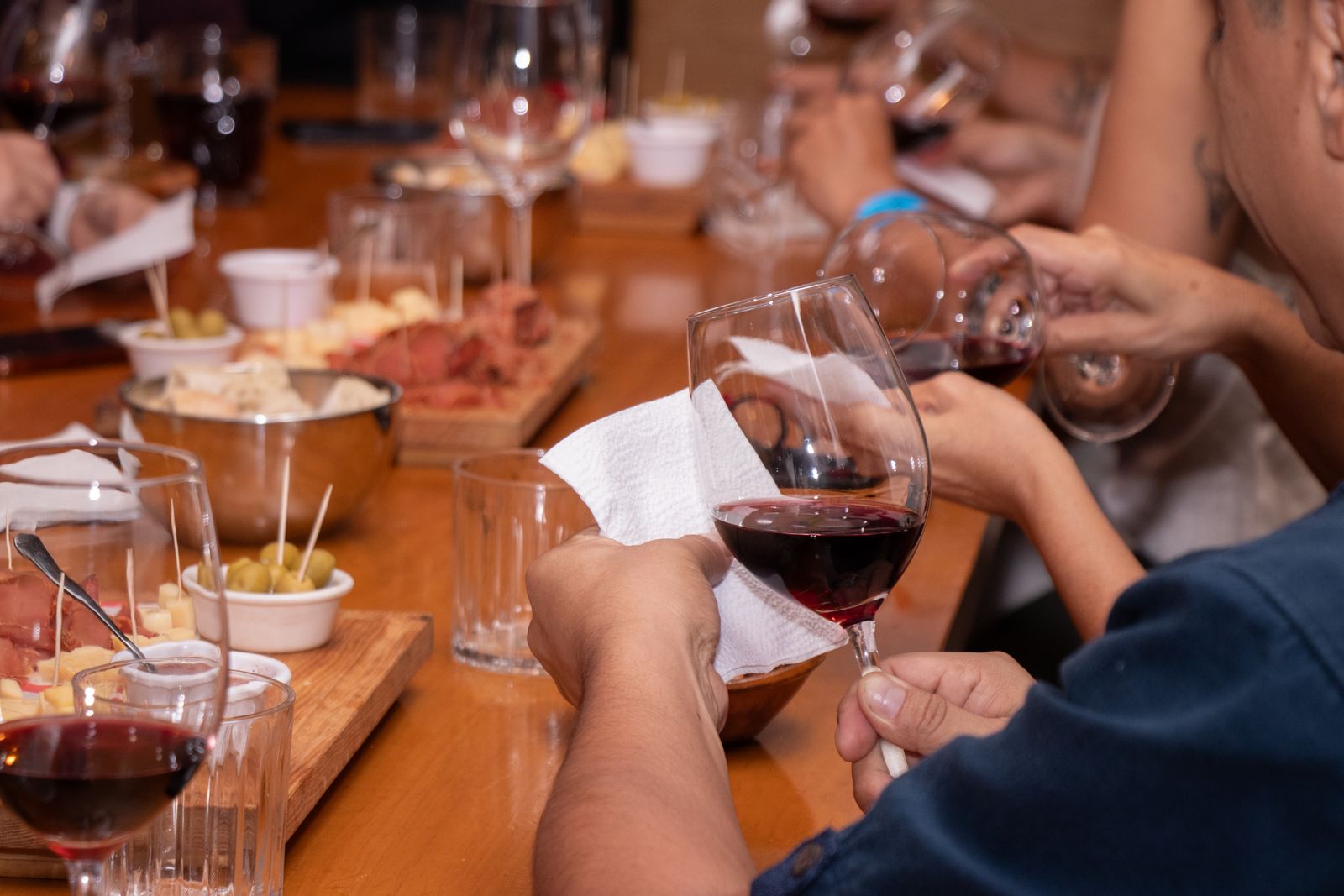 Hands holding glasses of red wine around a tasting table with small plates