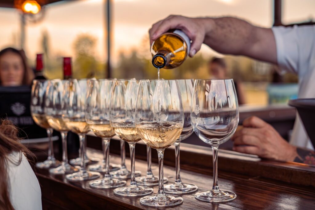White wine poured into glasses on a wooden counter at sunset
