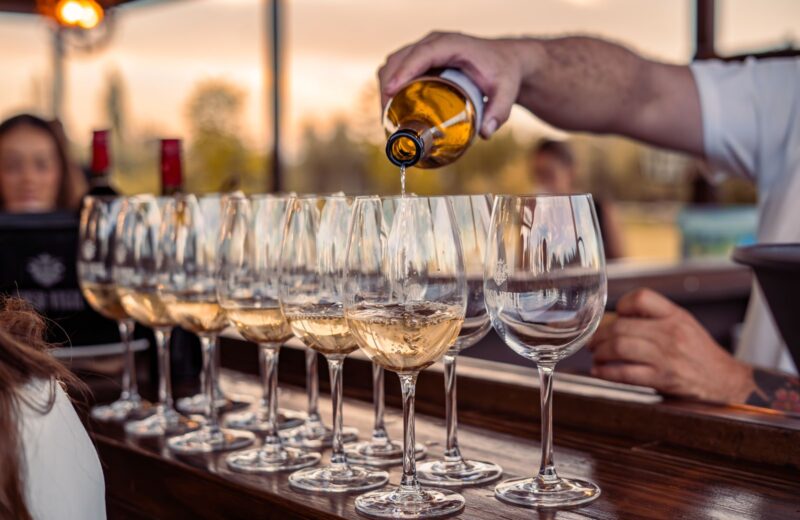 White wine poured into glasses on a wooden counter at sunset
