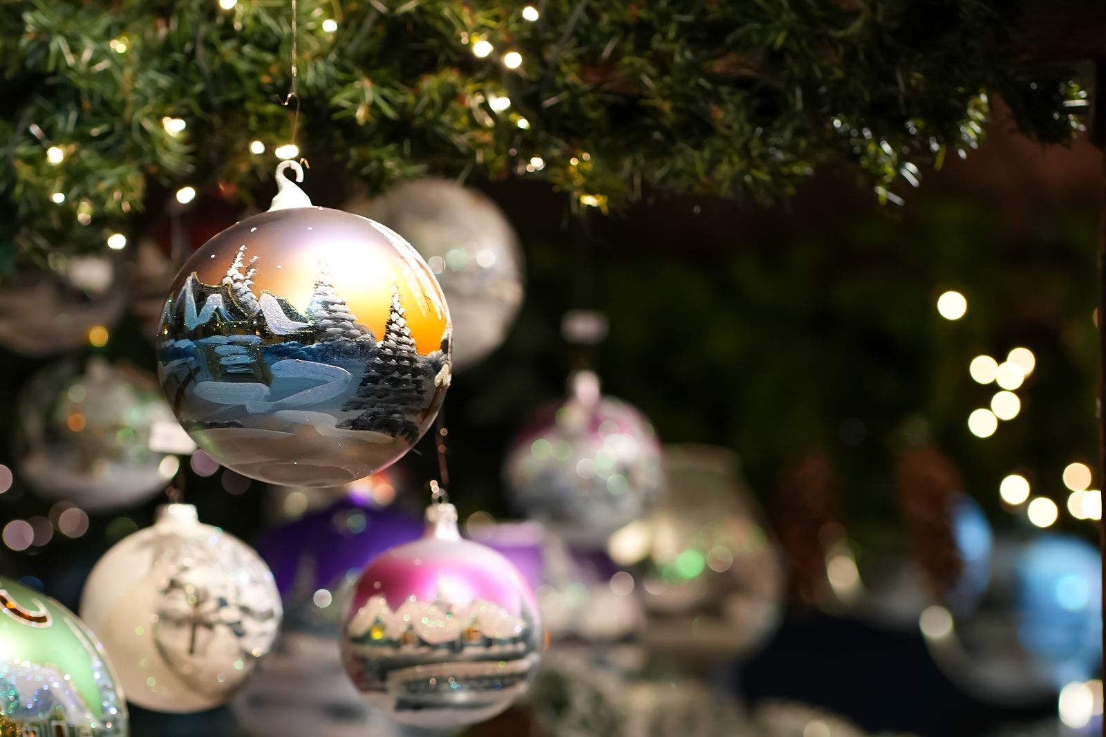Painted glass baubles with a winter village scene hanging on a Christmas tree