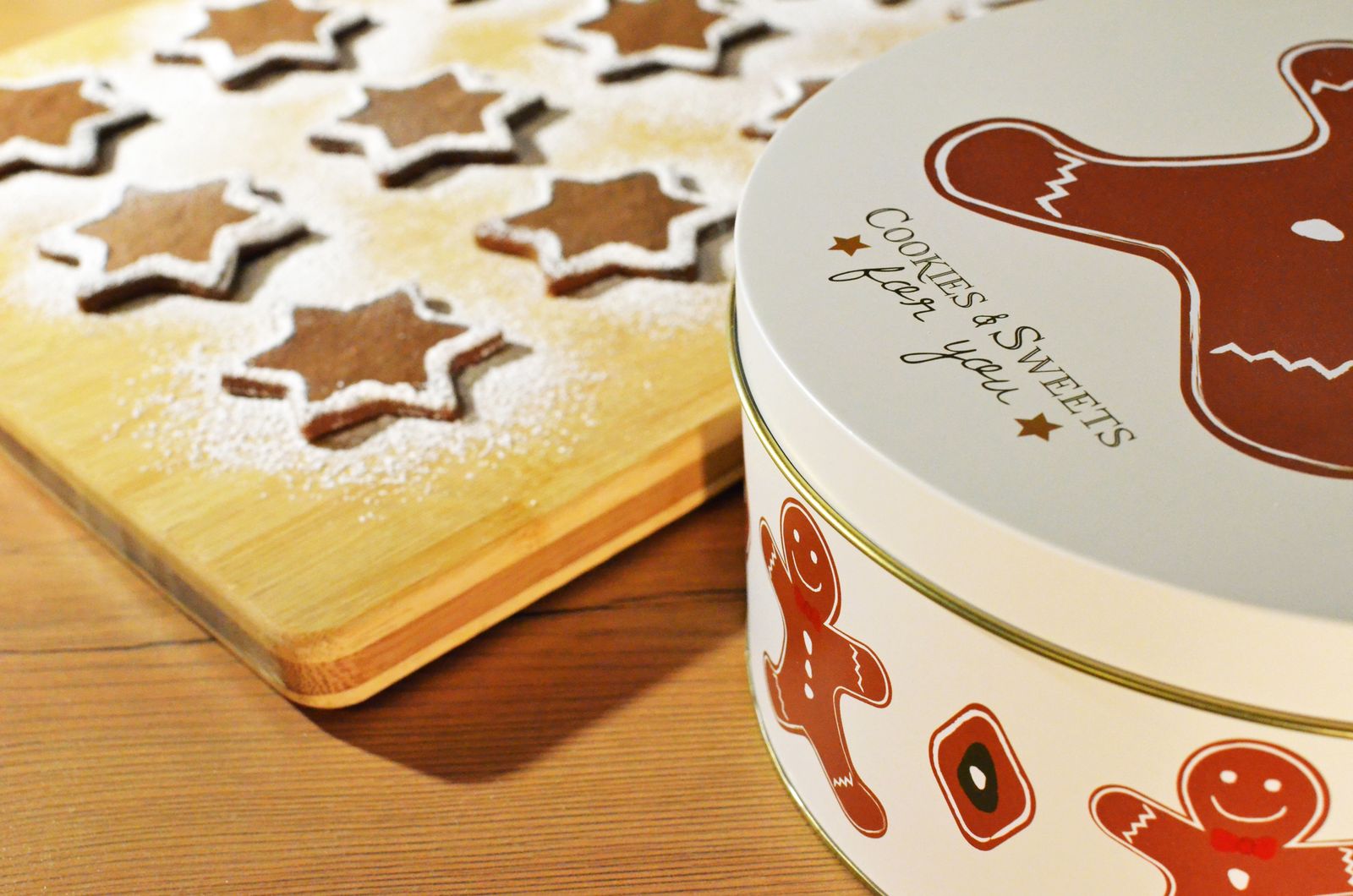 Star-shaped gingerbread biscuits dusted with sugar next to a gingerbread biscuit tin