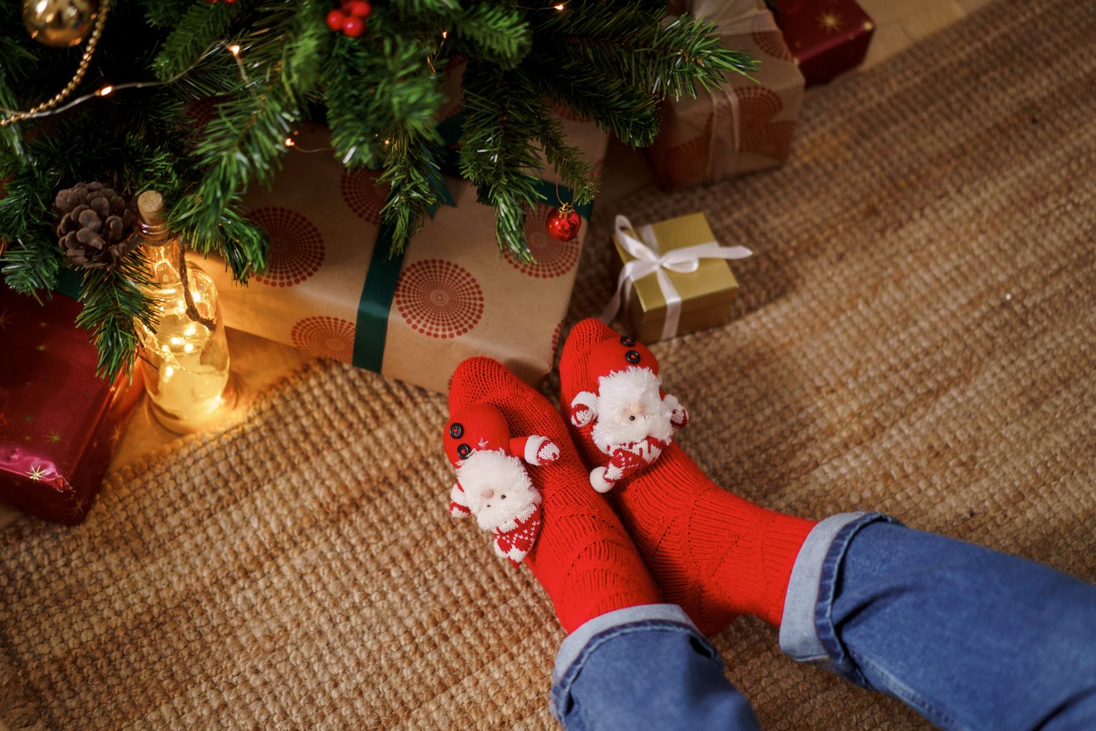 Feet in red Christmas socks on a rug beside wrapped presents under the tree