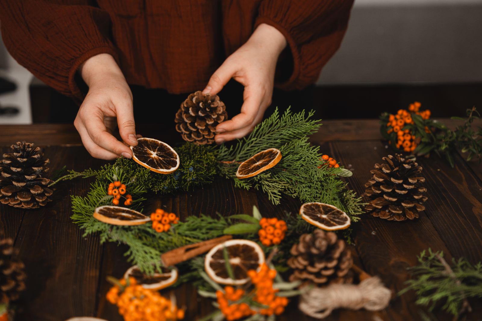 Hands placing pine cones and dried orange slices on a fresh fir wreath